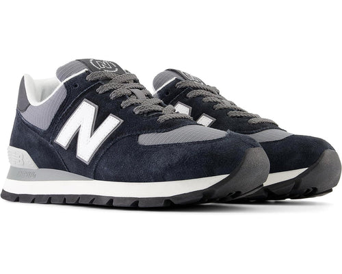 New Balance 574 Rugged sneakers in navy blue suede and gray ripstop material with white branding and durable outsole, angled front view.