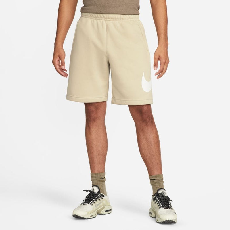 Nike Sportswear Club Shorts in beige with elastic waistband and white Nike Swoosh logo on left leg, front view.
