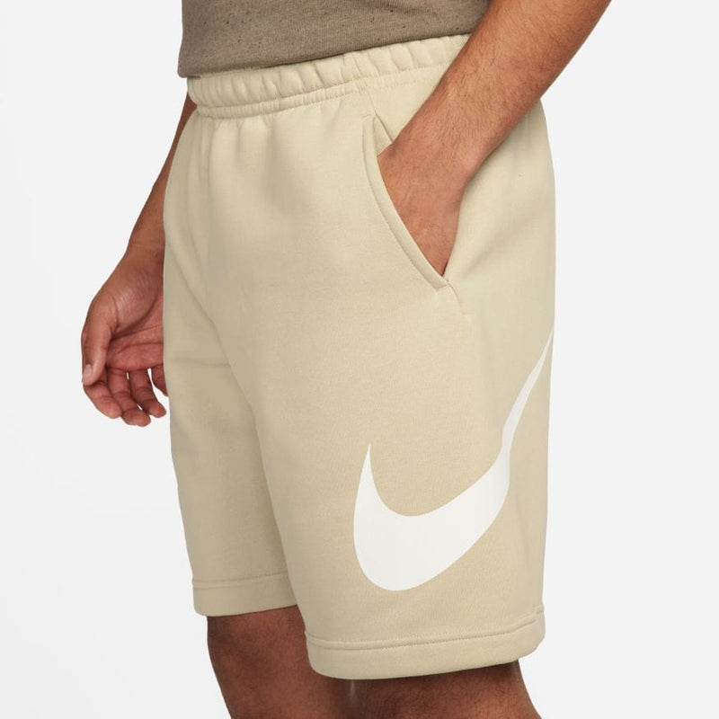 Nike Sportswear Club Shorts in beige with white logo, featuring elastic waistband and side pockets, front view.